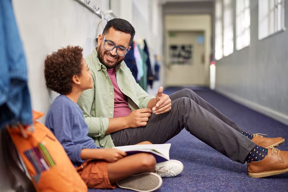 Ein Schulbegleiter unterhält sich mit einem Jungen auf dem Schulflur sitzend.